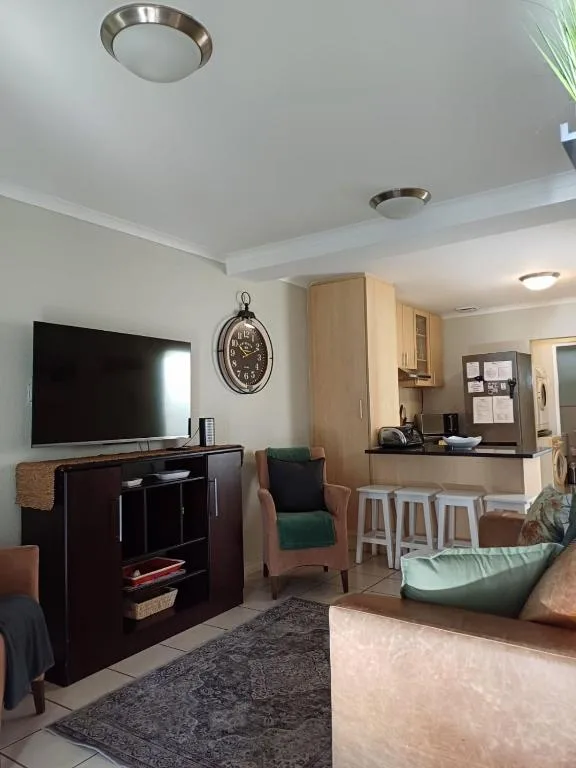 Open-plan lounge with TV, seating, and kitchen visible in background