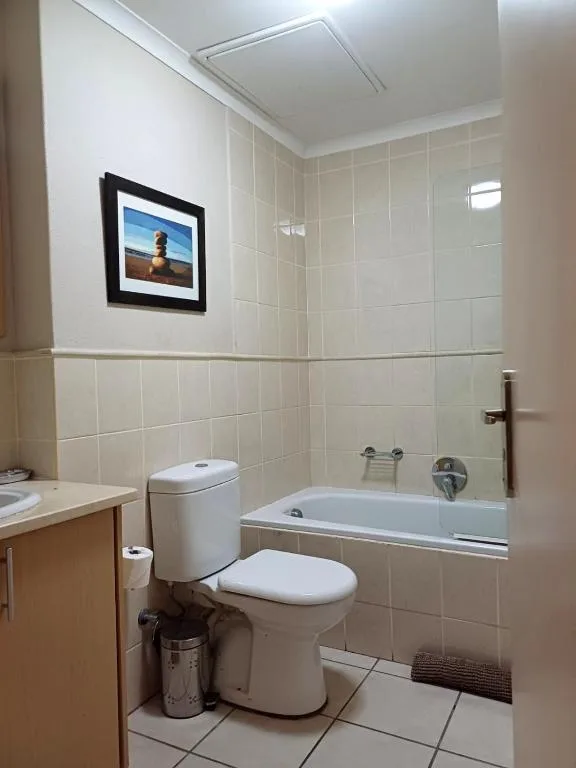 Clean bathroom with toilet, bathtub, and cream tiled walls