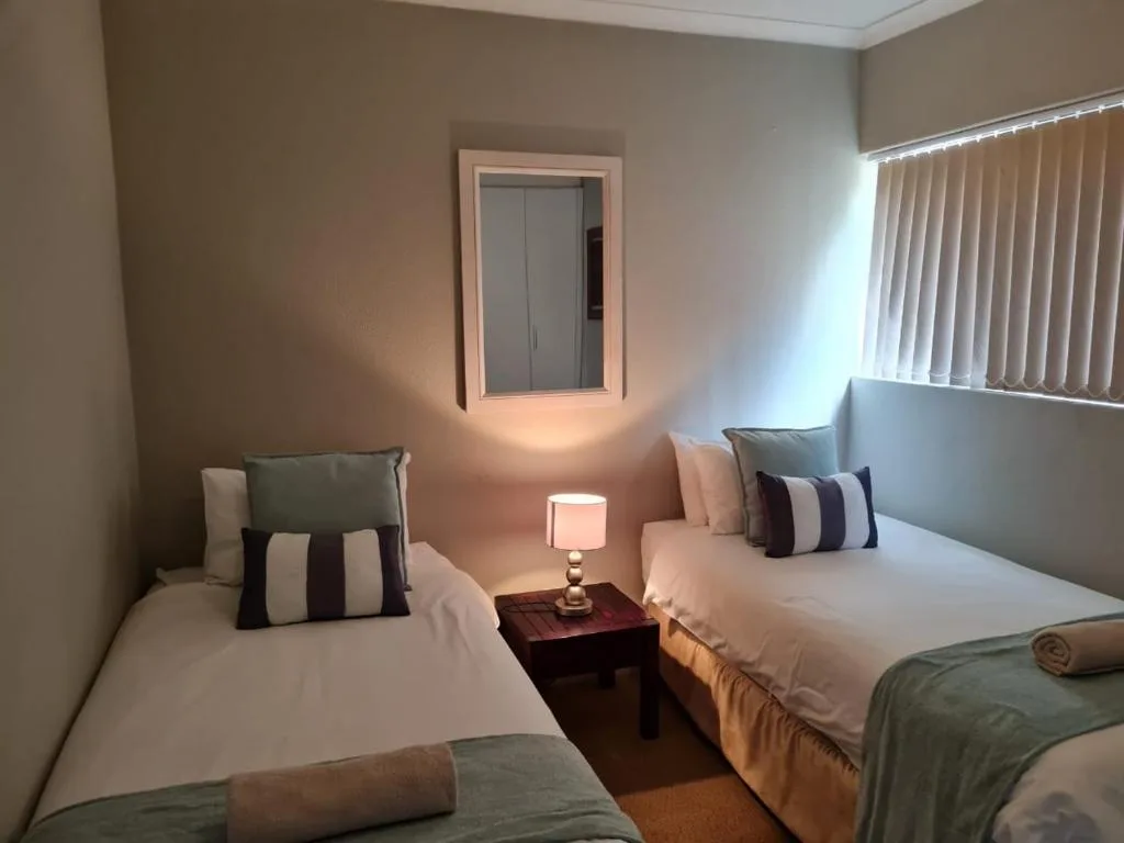 Twin bedroom with white linens, striped pillows, bedside lamp, and vertical blinds