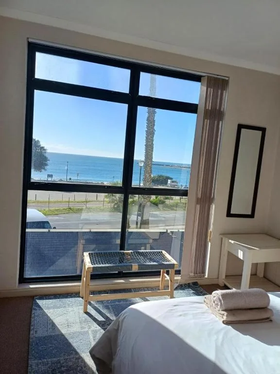 Bedroom with ocean view through large black-framed windows and palm tree
