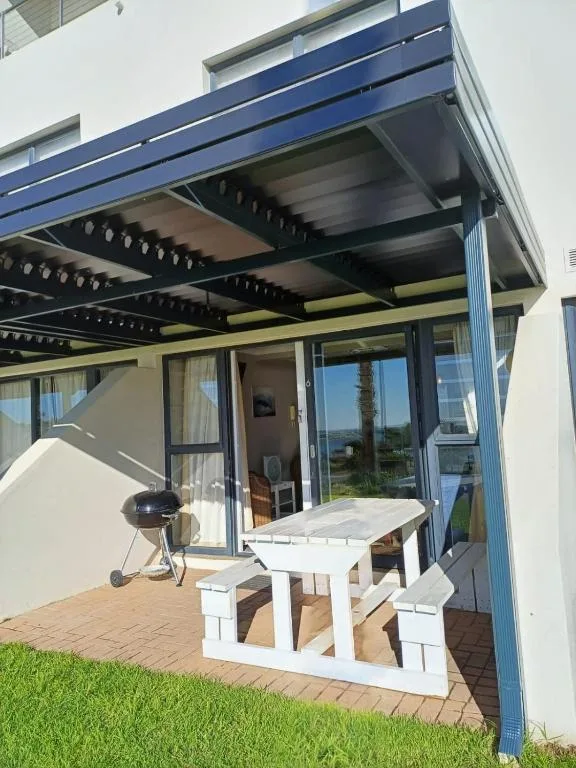 Modern patio with pergola, white picnic table, and braai grill overlooking garden