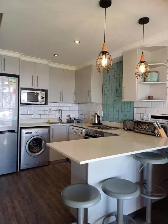 Modern kitchen with white cabinetry, teal tile backsplash, pendant lights