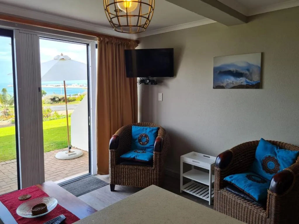Bright living room with wicker seating, blue cushions, wall-mounted TV, and ocean views