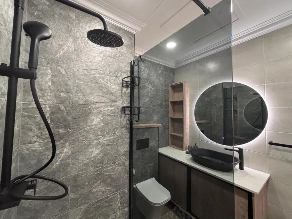Modern bathroom with rainfall shower, round illuminated mirror, and marble tiling