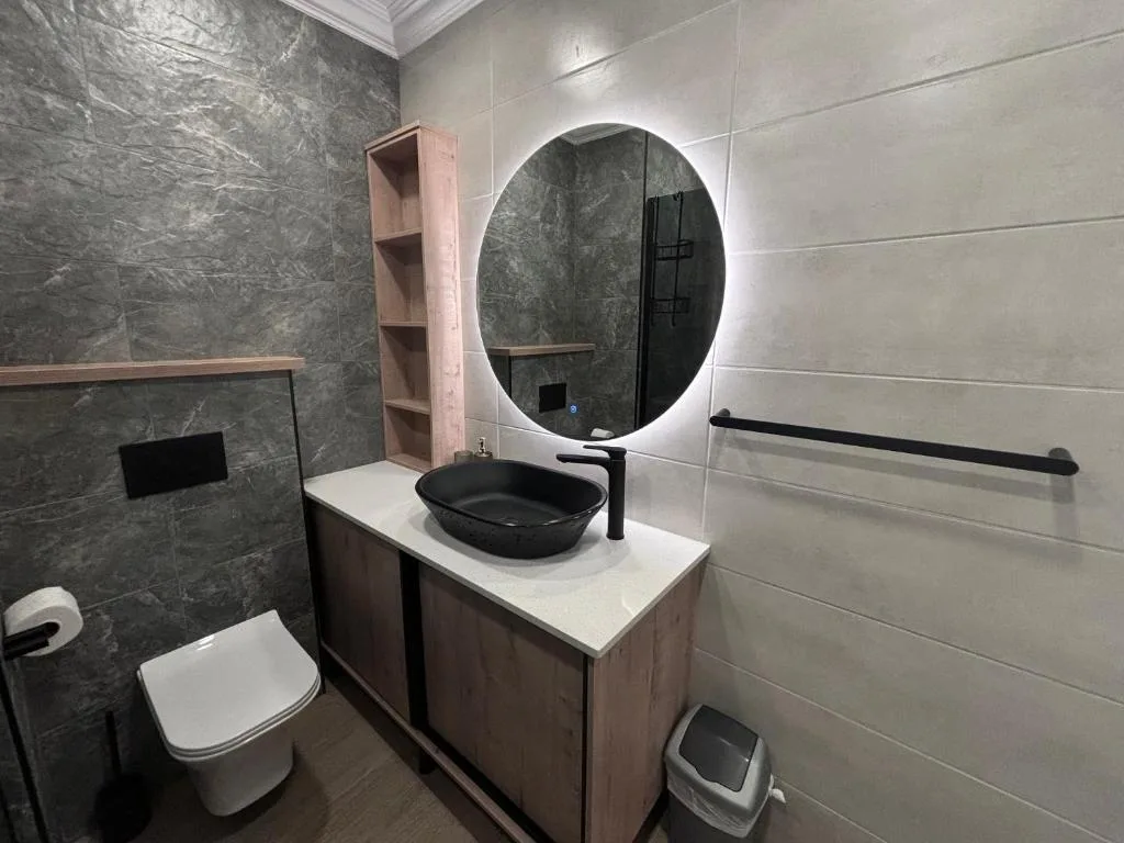 Modern bathroom with black bowl sink, illuminated oval mirror, and tiled walls
