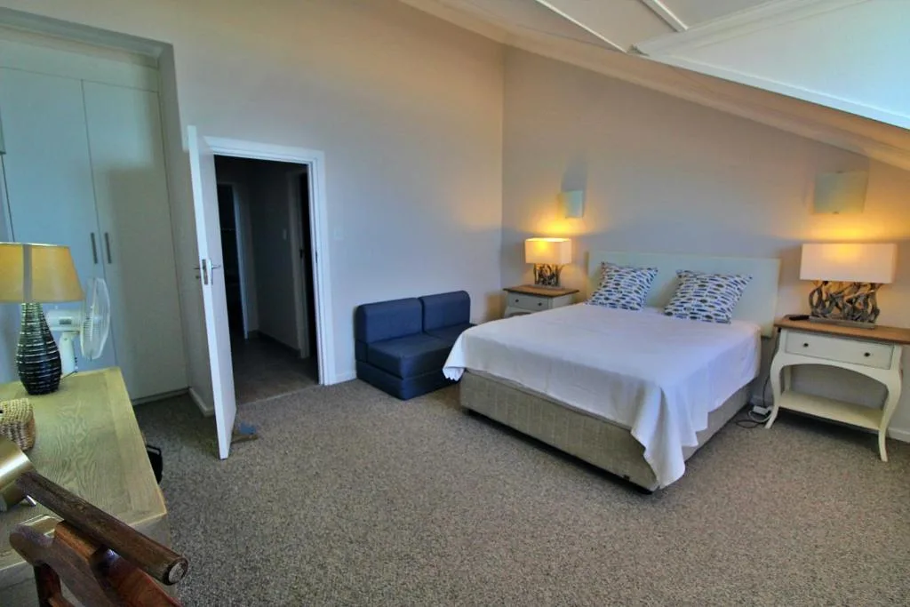 Spacious bedroom with queen bed, bedside lamps, and blue seating area