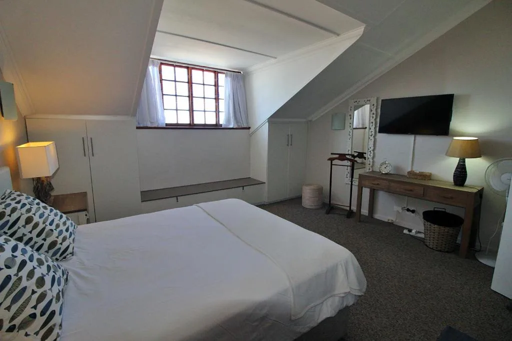 Spacious attic bedroom with queen bed, vanity, TV and sloped ceiling