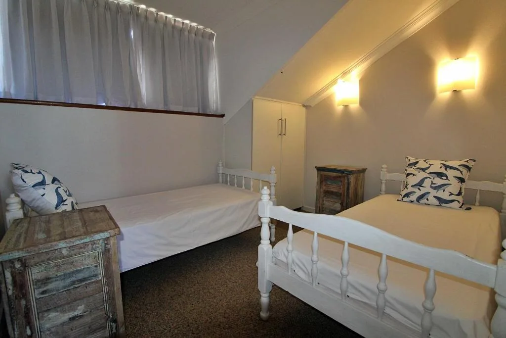 Bright bedroom with two white beds and nautical-themed cushions