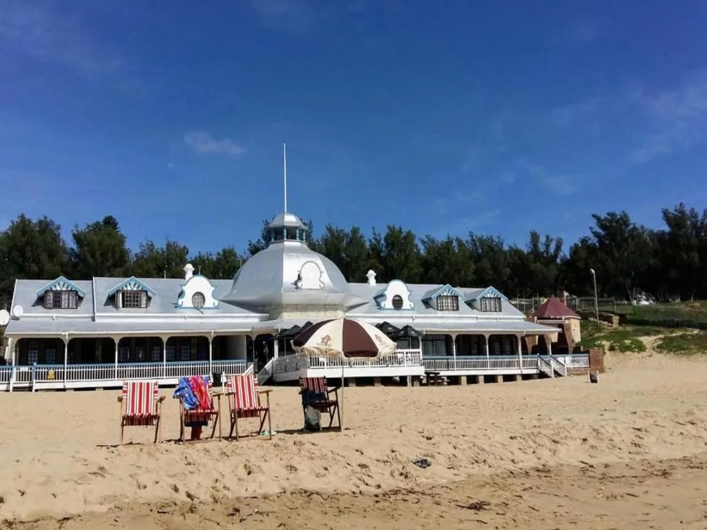 Victorian-style beachfront pavilion with distinctive dome, wide veranda, and sandy beach foreground