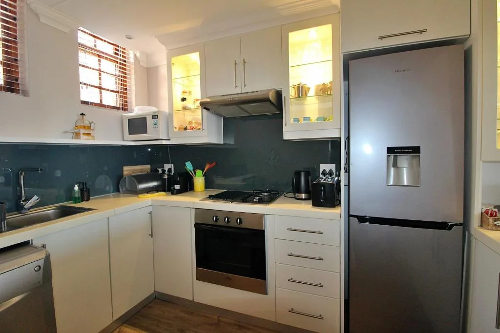 Modern kitchen with white cabinetry, stainless steel appliances, and teal backsplash