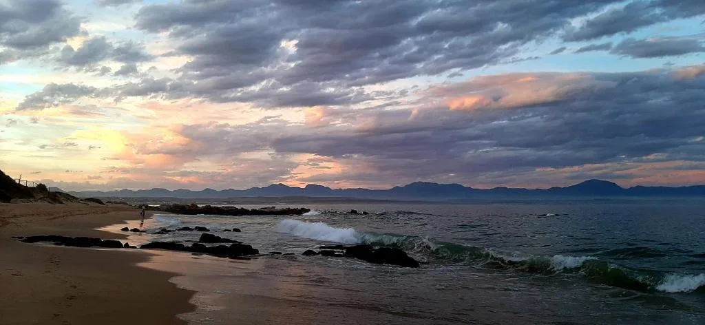 Dramatic sunset over ocean with mountains and sandy beach with waves