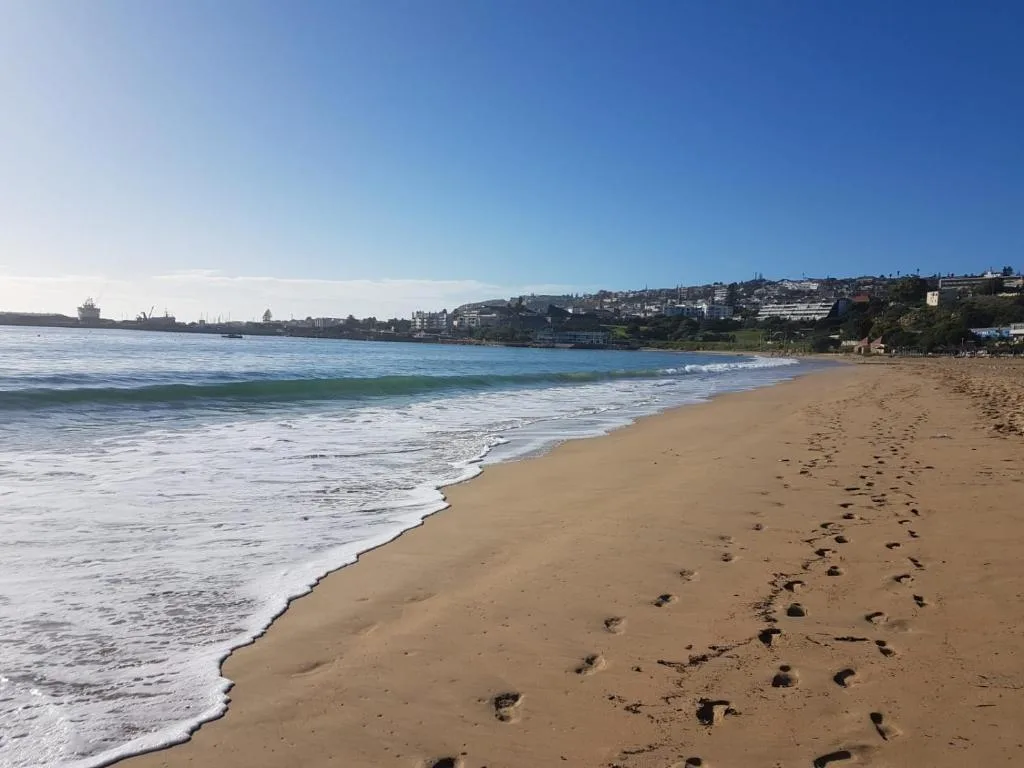 Sandy beach with ocean waves and coastal town hillside in background