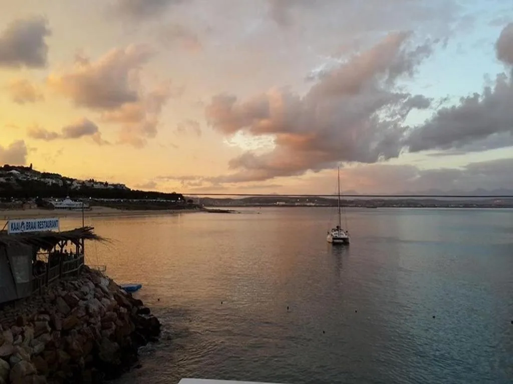 Sunset over Mossel Bay lagoon with sailboat and coastal restaurant visible