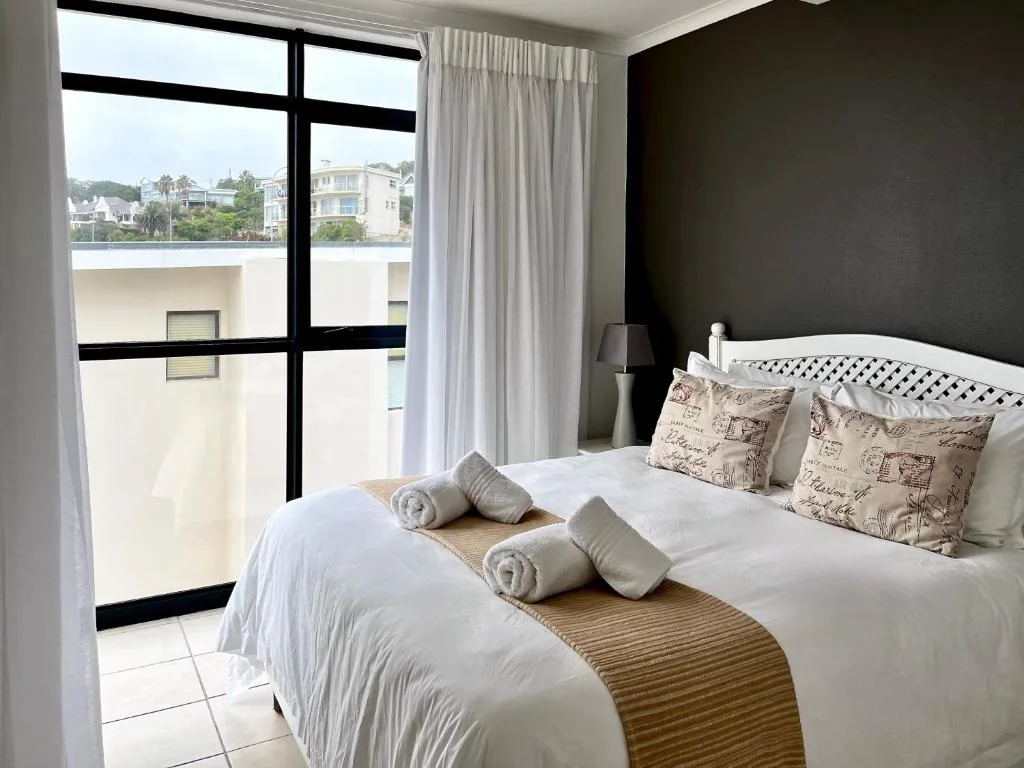 Modern bedroom with double bed, rolled towels, and sliding door overlooking town