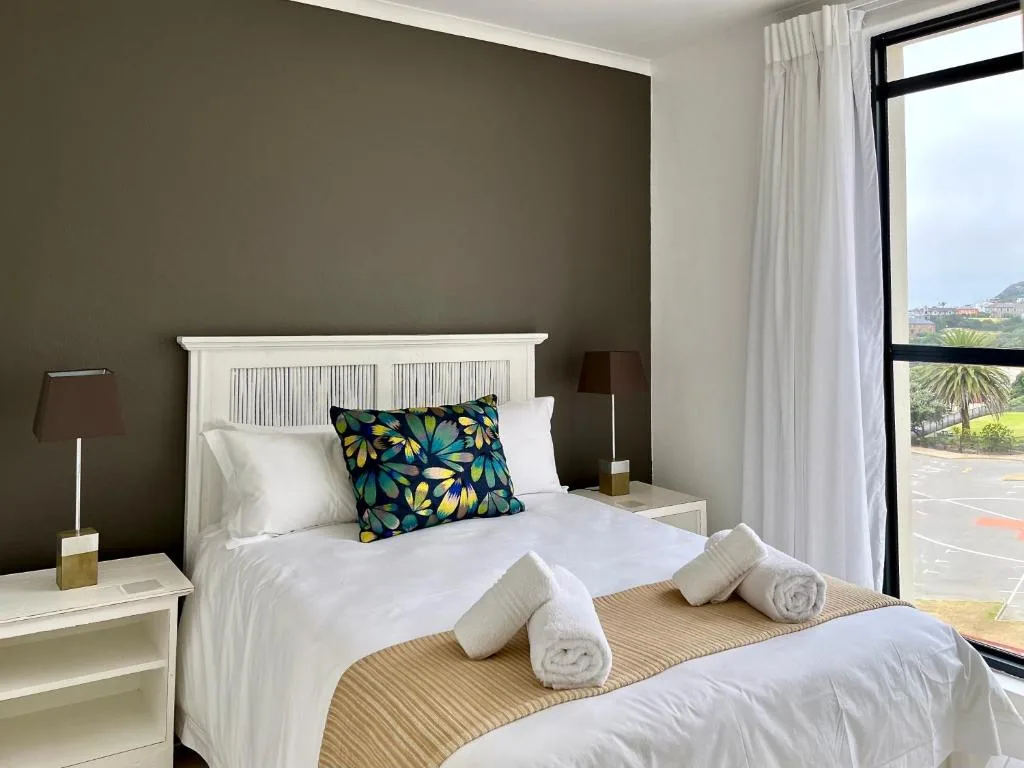 Modern bedroom with white bed, colorful floral pillows, and garden view