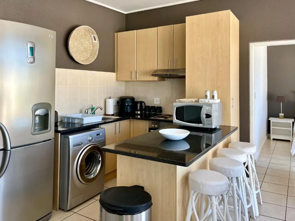 Modern kitchen with light wood cabinetry, black countertop, and stainless steel appliances