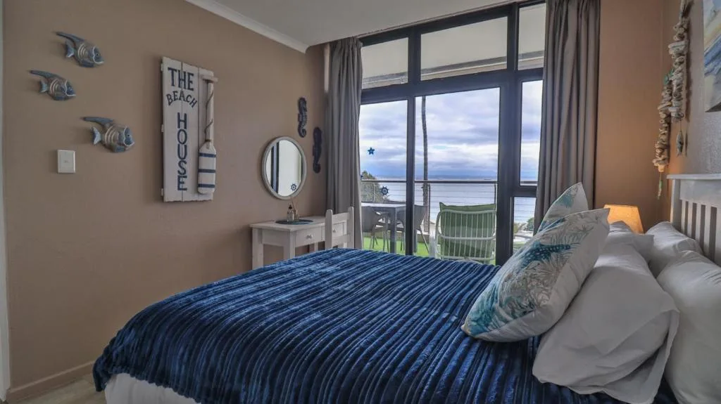 Coastal bedroom with blue striped bedding and waterfront views through glass doors