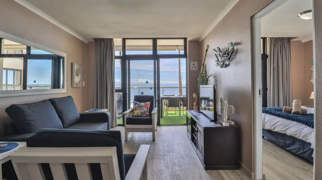 Modern lounge with black sofa, ocean views through large windows, and adjacent bedroom