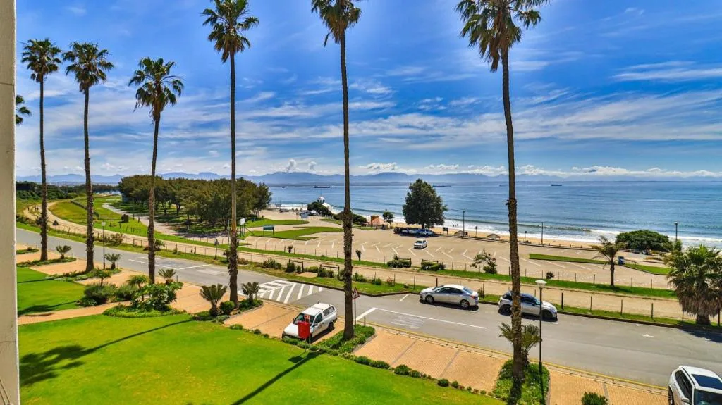 Scenic coastal view with palm trees, beach, and mountains in distance