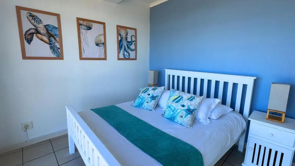 Bright blue bedroom with white bed frame and ocean-themed wall art
