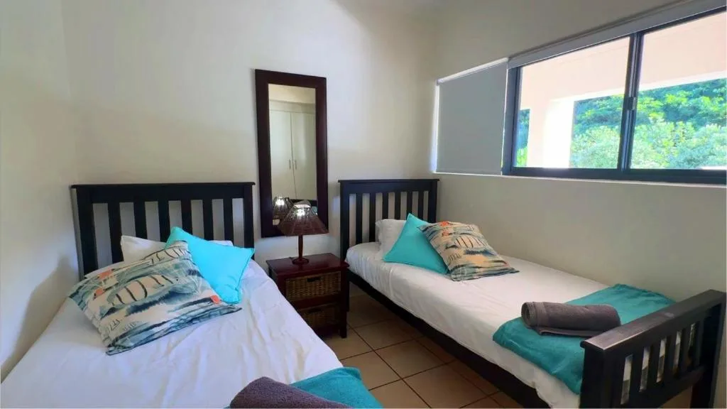 Twin bedroom with black wooden beds, turquoise pillows, and garden views