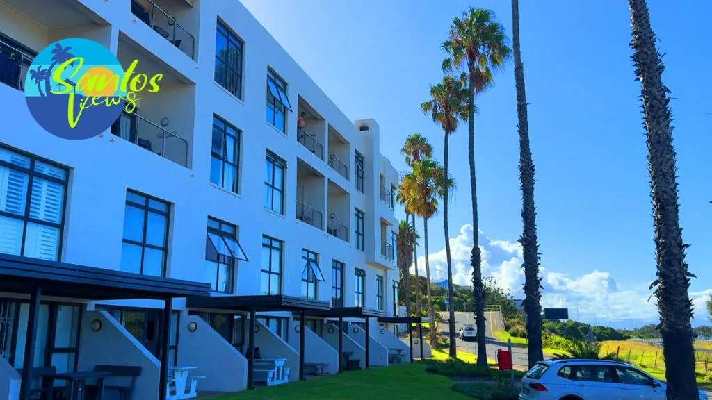 Modern blue and white apartment building with palm trees and green lawn