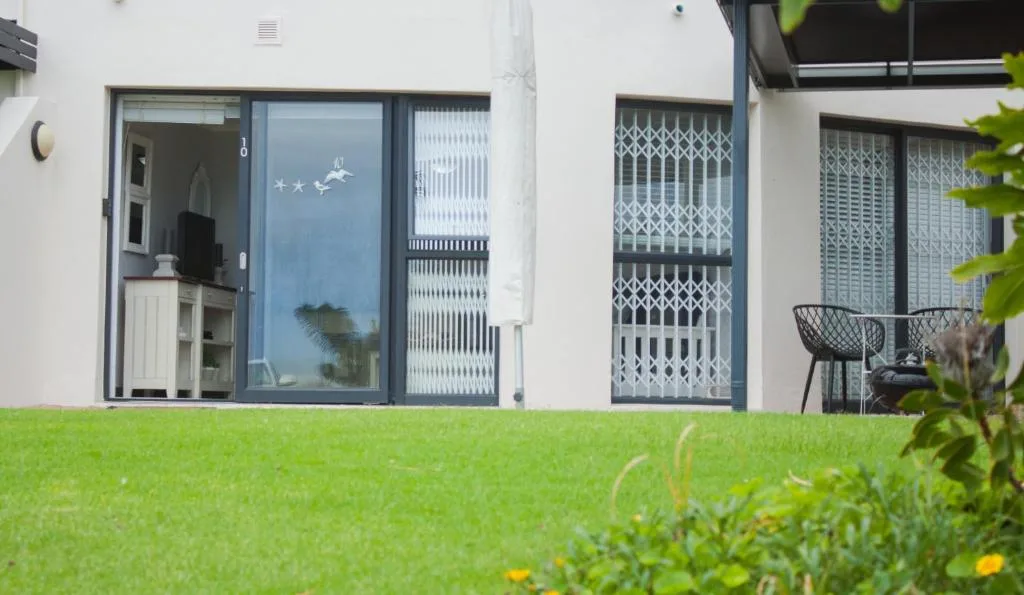 Modern white apartment facade with blue-framed doors and manicured green lawn