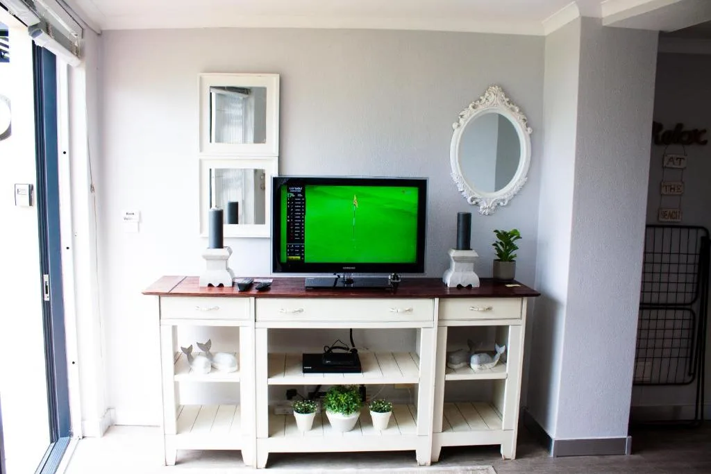 Modern lounge with TV mounted above white storage unit and decorative mirror