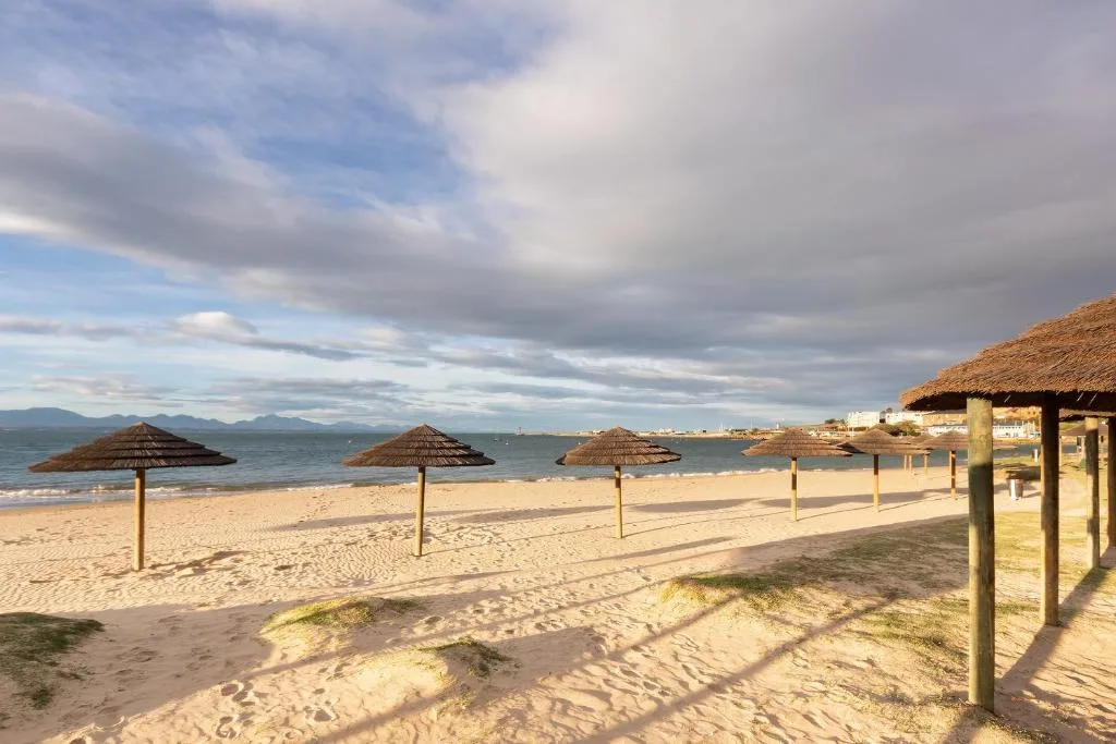 Scenic beachfront with thatched umbrellas, golden sand, and mountains beyond