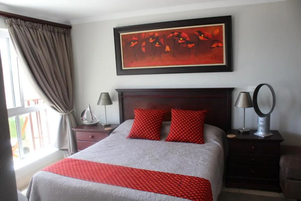 Stylish bedroom with dark wood bed, red patterned pillows, and modern artwork