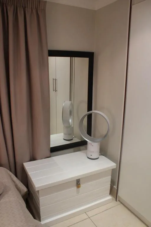 Bedroom vanity with mirror, white drawers, and portable fan