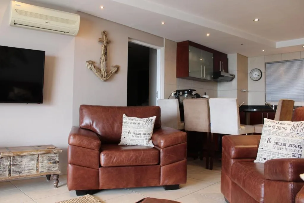 Open-plan lounge with brown leather armchairs, TV, and kitchen visible