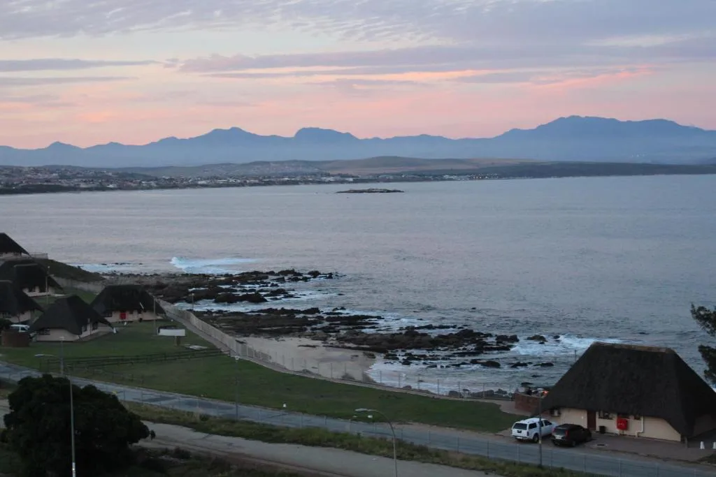 Sunset view over bay with mountains, coastal town, and rocky shoreline