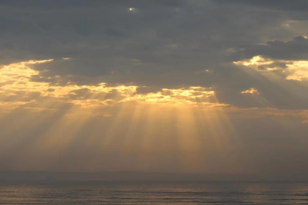 Dramatic sunset over ocean with golden light rays breaking through clouds
