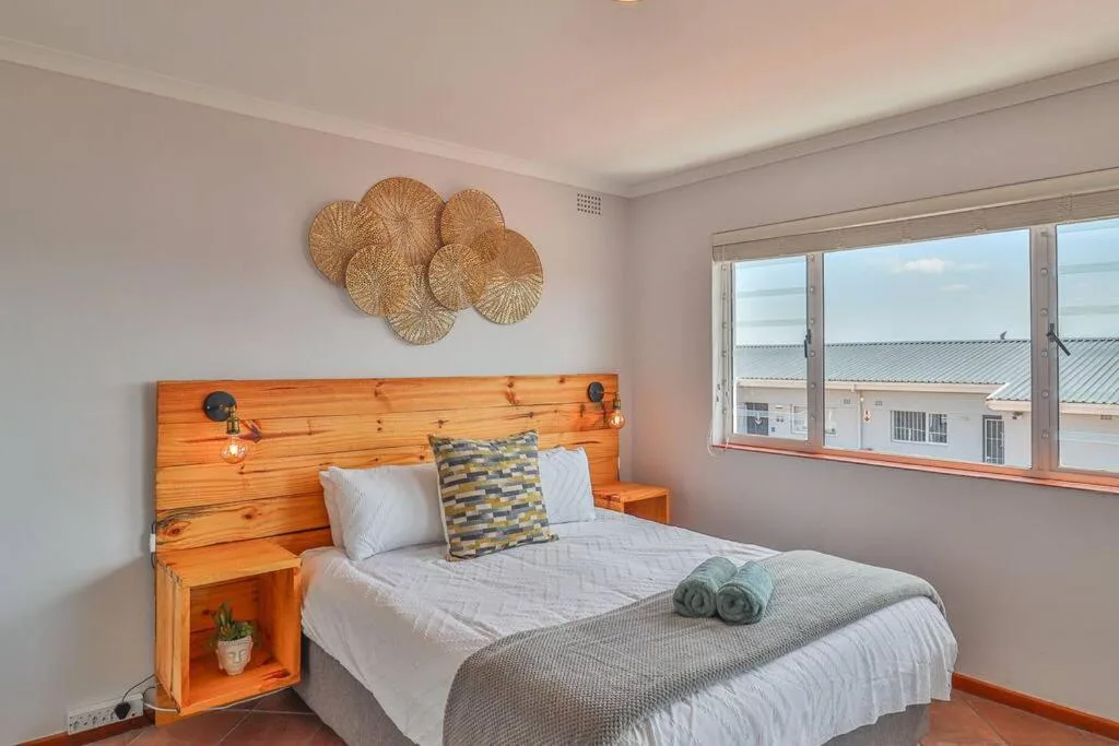 Bright bedroom with wooden headboard, white bedding, and woven wall decor