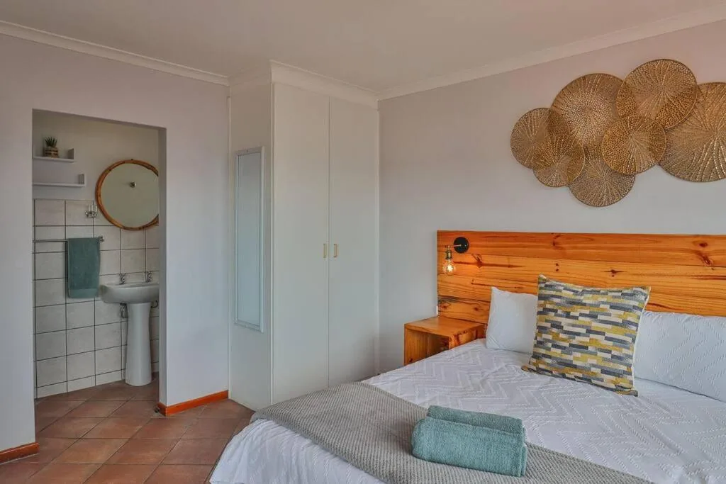 Bright bedroom with wooden headboard, en-suite bathroom visible, woven wall decor