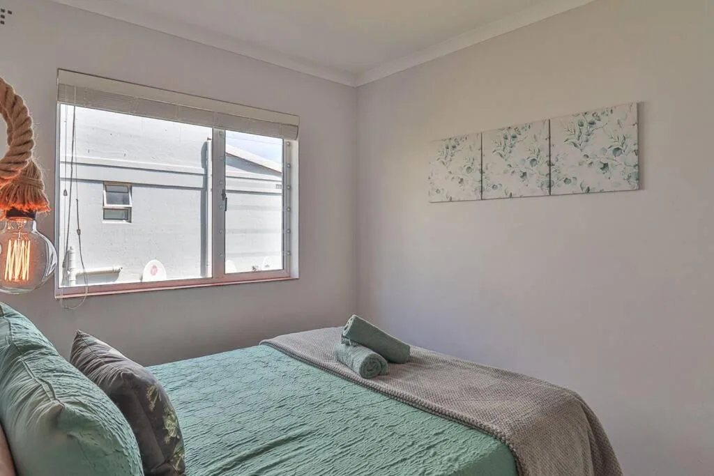 Bright bedroom with double bed, green bedding, wall art, and window