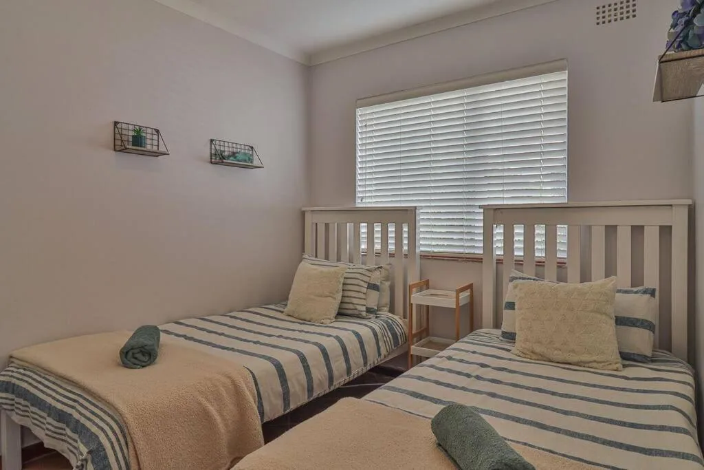 Twin bedroom with striped bedding, wooden cots, and shuttered window