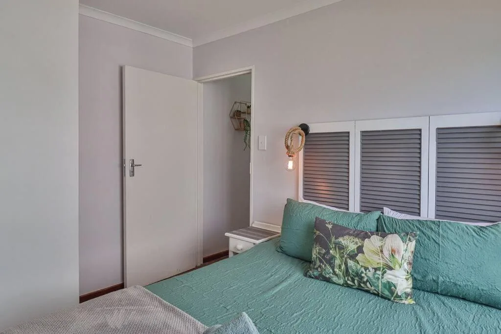 Bright bedroom with green quilted bed, louvered doors, and ensuite entrance