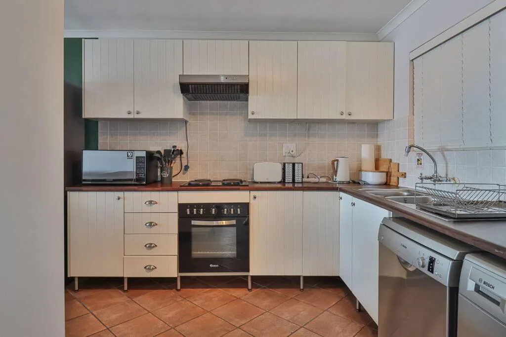 Compact kitchen with cream cabinetry, black oven, and terracotta floor tiles