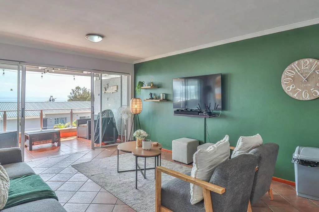 Living room with green accent wall, TV, comfortable seating, and ocean views through sliding doors