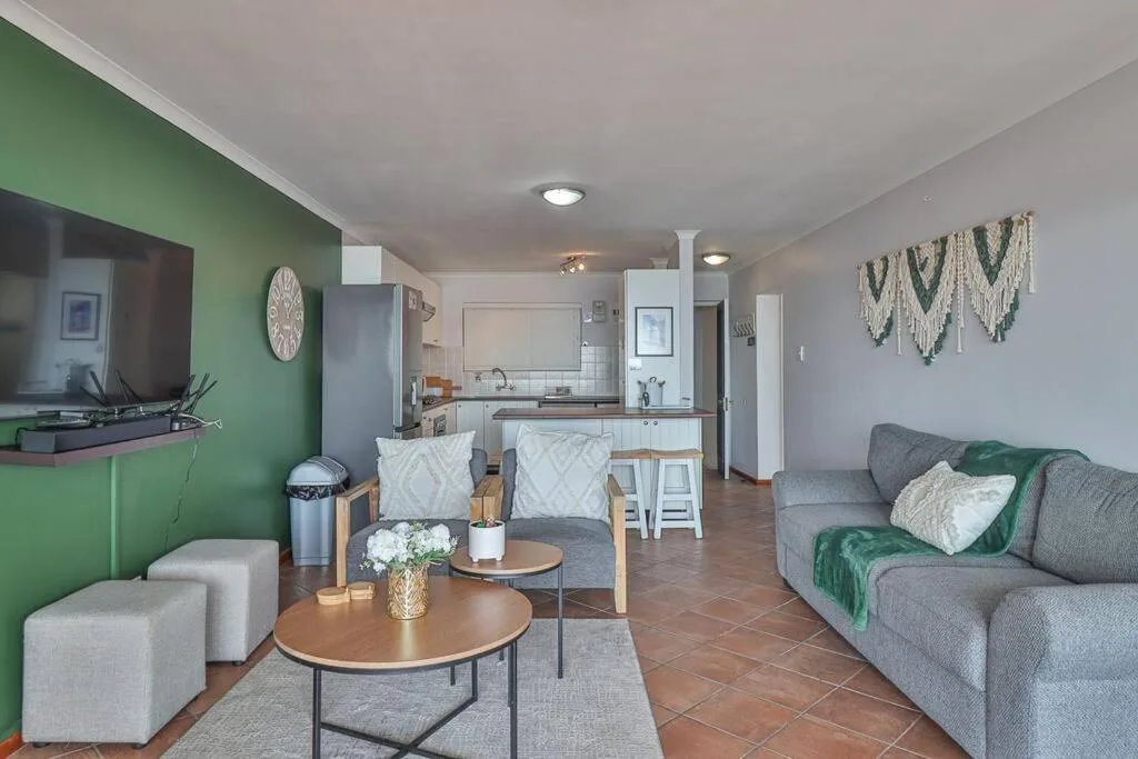 Open-plan lounge with gray sofa, green accent wall, and kitchen visible beyond
