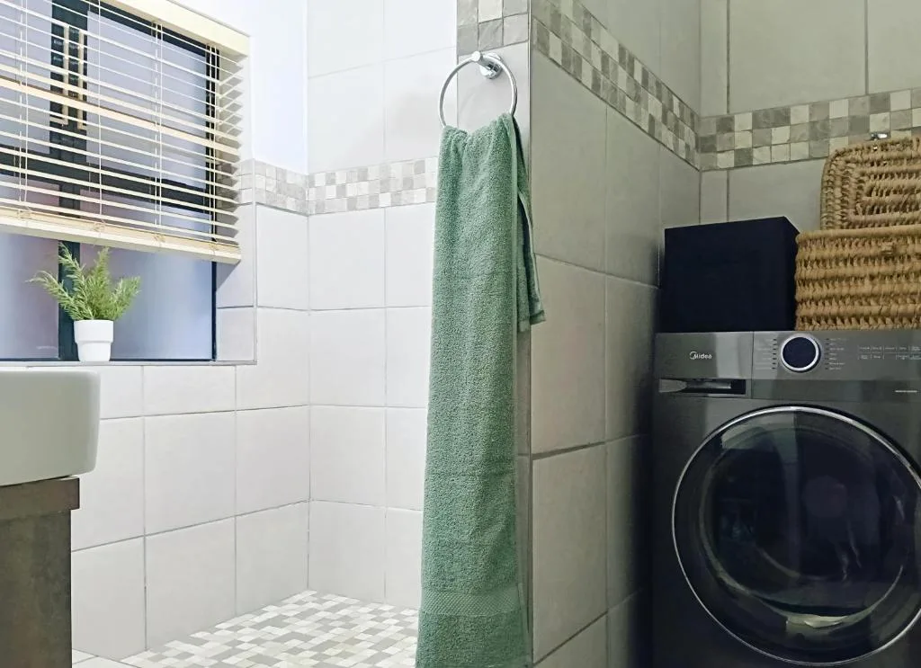 Modern bathroom with walk-in shower, washer-dryer, white tiles, and green towel