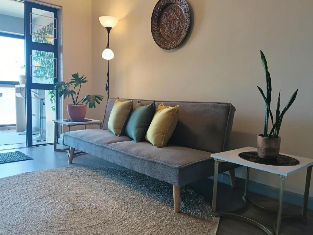 Modern lounge with gray sofa, colorful pillows, potted plants, and natural light