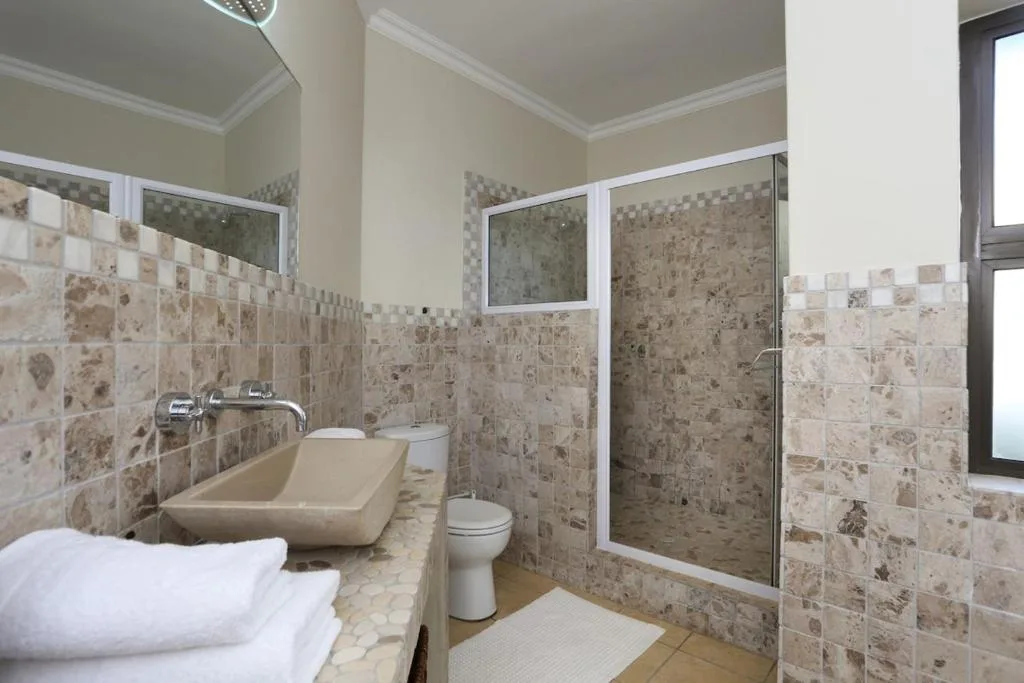 Modern bathroom with travertine tile walls, double vanity, and enclosed shower