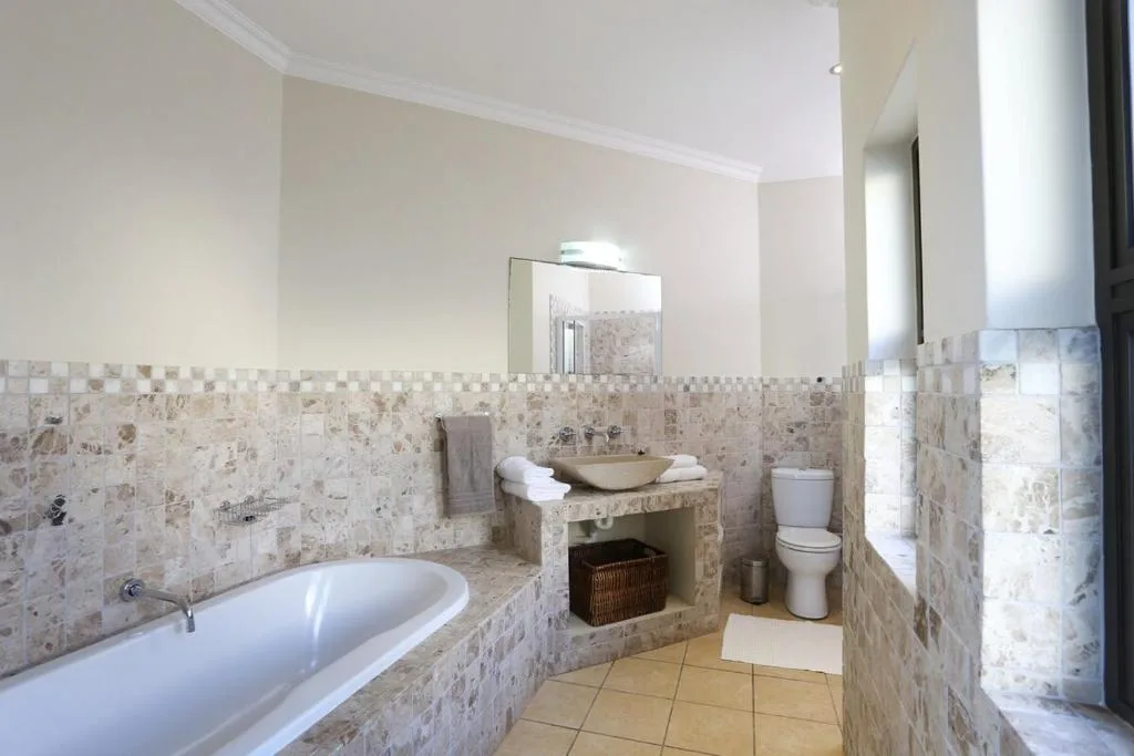 Spacious bathroom with bathtub, vanity sink, toilet, and travertine tiling
