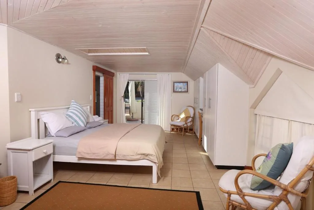 Spacious bedroom with white bed, skylight ceiling, and comfortable seating area