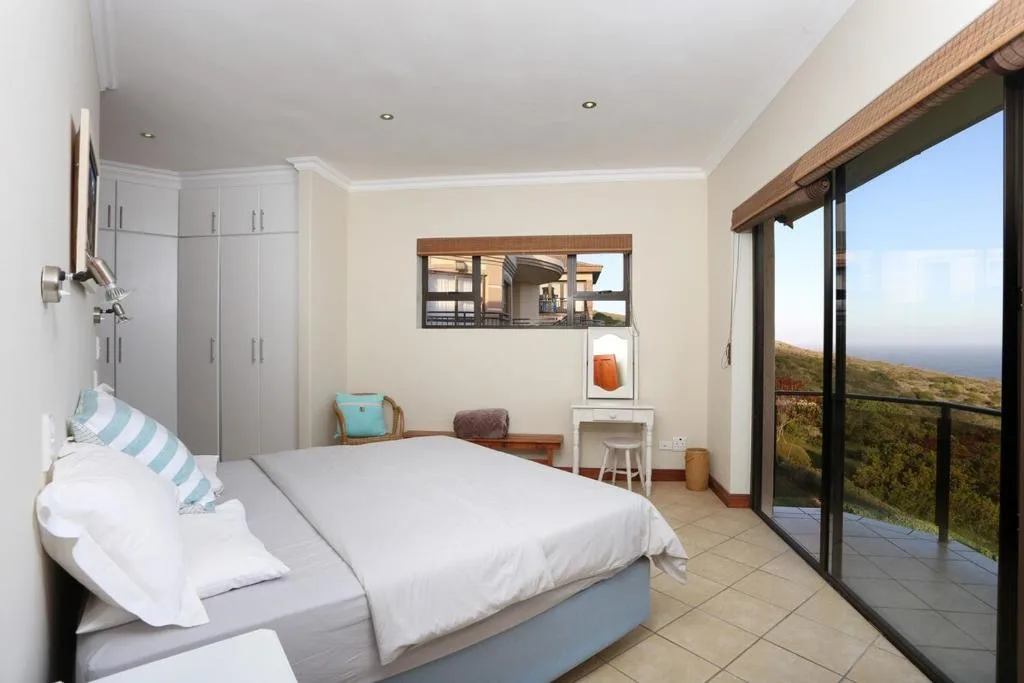 Bright bedroom with white bedding, ocean view doors, coastal landscape visible outside