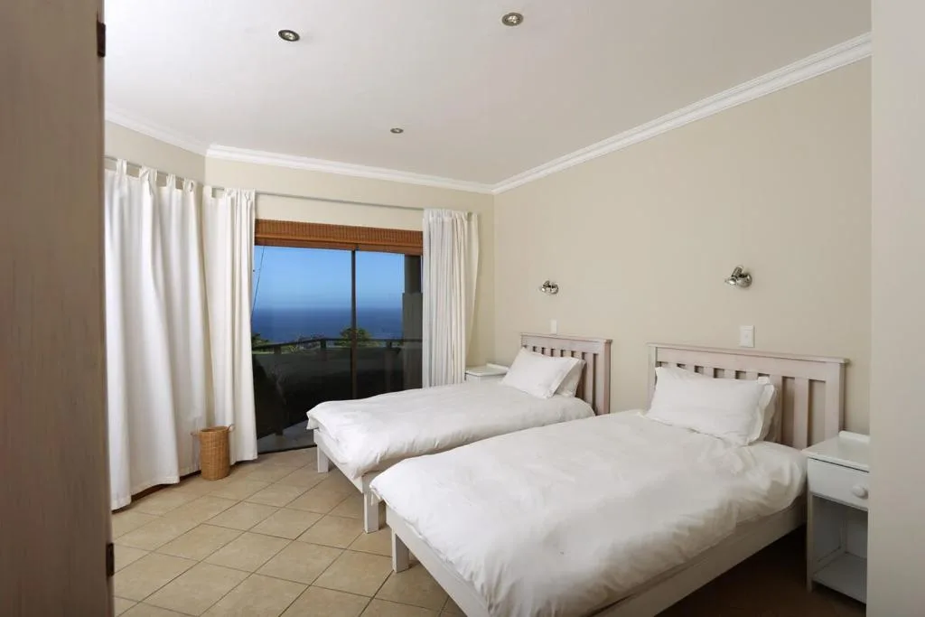 Twin bedroom with ocean view through sliding glass doors and white bedding