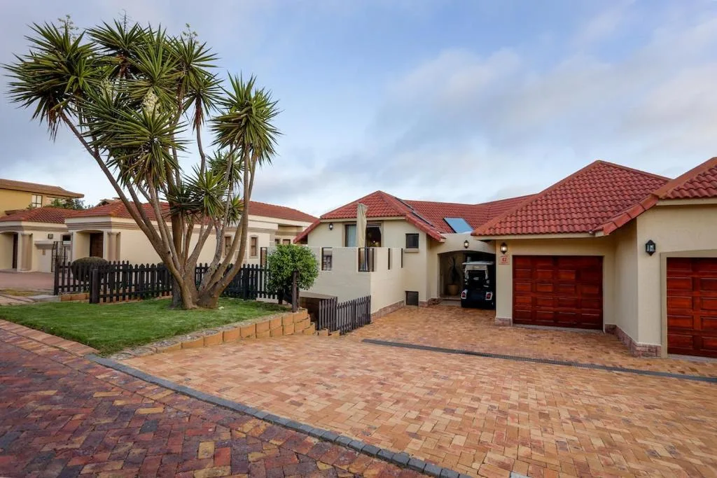 Modern villa with red tile roof, brick driveway, and tropical palm tree landscaping